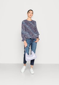 Blusa estampada com flores em azul marinho com detalhes em vermelho e branco, jeans de ganga, ténis brancos e uma bolsa texturizada em lavanda.