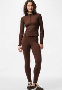 Ruda ilgomis rankovėmis sportinė palaidinė su priekinio užtrauktuko detalėmis, derinama su atitinkančiomis prigludusiomis tamprėmis. Lygi tekstūra, glaudus siluetas, skirtas aktyviam dėvėjimui.