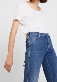 Camiseta blanca y ligera de manga corta combinada con jeans de mezclilla ajustados de color azul oscuro. Los jeans tienen un diseño clásico y costuras sutiles.