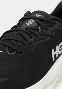 Baskets de sport noires avec une tige en tissu texturé, de grosses lacets et un logo blanc. Elles sont dotées d'une semelle rembourrée et d'éléments de design épurés.
