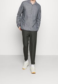 Szara koszula w wzory z kołnierzykiem, zapinana na guziki, z długimi rękawami, zestawiona z ciemnoszarymi spodniami w kratę i białymi trampkami.