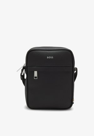 Black synthetic crossbody bag with smooth texture, silver logo, adjustable strap, and a zippered compartment. Compact square shape.
