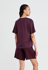 Burgundy short-sleeve top with a relaxed fit, paired with matching shorts. Made from soft fabric, featuring minimal design and no visible logos.