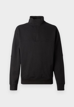 Black fleece pullover with a high collar, half zip, and ribbed hem. Features a subtle logo on the chest and wide sleeves. Smooth texture.