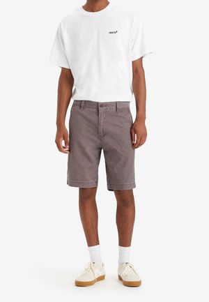 Grå bomuldsshorts med et klassisk snit, kombineret med en hvid t-shirt med rund hals og et lille sort logo samt hvide sokker og sneakers.