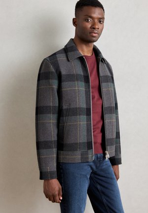 Gray and black plaid jacket with green accents, structured collar, front zipper, and two side pockets. Paired with a maroon sweater and blue jeans.