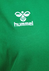 Zielona bawełniana koszulka z białym haftowanym logo Hummel i stylizowanym wzorem pszczoły umieszczonym na środku klatki piersiowej.