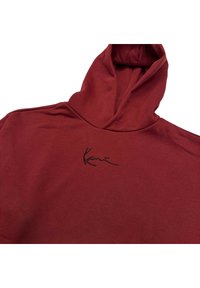 Sudadera de algodón roja con un bolsillo canguro frontal y una firma bordada en negro. Presenta una capucha estructurada y una textura suave.