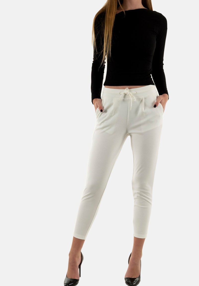 Pantalon blanc ajusté avec taille élastique et cordon de serrage, doté de deux poches avant, associé à un haut noir à manches longues et des talons noirs.