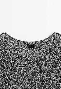 Black and white knitted cotton sweater featuring a wide crew neckline and a textured pattern. Brand label visible on the neck.