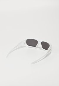 Λευκά γυαλιά ηλίου με σκούρους φακούς, διαθέτοντας αεροδυναμικό σχεδιασμό και υφασμάτινα διακοσμητικά στοιχεία στη μπορντούρα. Λογότυπο brand σε χρυσό σε ένα από τα χέρια.