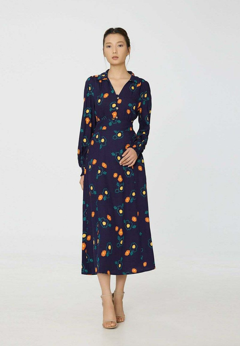 Robe à manches longues marine avec un décolleté en V, ornée de motifs floraux orange et turquoise. Fabriquée en tissu léger, elle présente une taille cintrée et une jupe fluide.