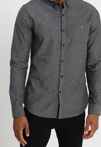 Grijs overhemd met lange mouwen en knopen, gemaakt van een gestructureerde stof, met een klein geborduurd logo op de borst en een klassieke kraag.