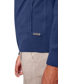 Pull en tricot bleu marine avec poignets et ourlet côtelés, doté d'une poche latérale et d'une petite étiquette métallique portant l'inscription « pierre cardin ».