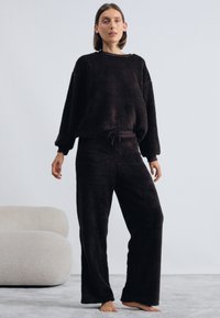 Melnā vilnas treniņtērpa komplekts, kas sastāv no brīva krekla ar platām piedurknēm un atbilstošām elastīgām biksēm. Mīksta tekstūra, minimālistisks dizains.