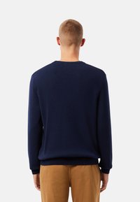 Suéter de punto azul marino con cuello redondo y mangas largas, con un dobladillo y puños acanalados, mostrado desde la parte trasera.