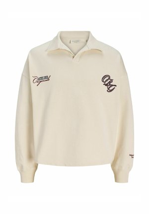 Polo beige à manches longues avec col ouvert, texte « Atelier Originals » sur la poitrine gauche, et broderie stylisée « OJC » sur la poitrine droite.