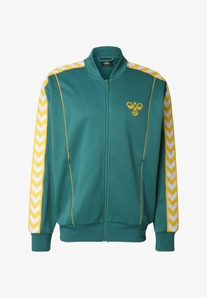 Tirkizna sportska jakna na patentni zatvarač sa žutim detaljima i bijelim cik-cak uzorkom na rukavima. Ima rebraste manžete i logo na prsima. Mekani materijal.