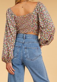 Floral kort topp med rynkad rygg och puffärmar; kombinerad med högmidjade, blekta blå jeans med bakfickor.