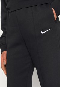 Black Nike sweatpants with an embroidered white logo. Made from soft fabric, featuring side pockets and a relaxed fit.