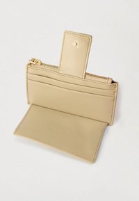 Bézs bőr pénztárca cipzáras záródással, belső kártyatartókkal és elülső füllel, amely aranyszínű díszítést visel, sima textúrával.