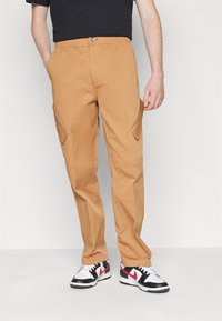 Bruna cargobyxor med en avslappnad passform, utrustade med sidofickor och elastisk midja. Matchade med svarta och vita sneakers.