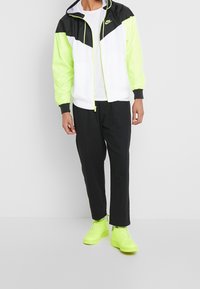 Nike vindjacka med en svart, vit och neongrön färgblockdesign, med elastiska mudd och en dragsko i huvan. Svarta byxor fulländar looken.