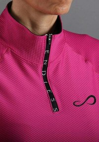 Close-up van een persoon die een textuur roze ritsopdracht draagt met een zwarte ritsstrip gelabeld "ENDLESS" en een zwart oneindigheidssymbool.