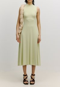 Minzgrünes ärmelloses Kleid mit eng anliegendem Oberteil, ausgestelltem Rock und gerippter Textur. Kombiniert mit einer klobigen beigefarbenen Schultertasche und braunen Riemchensandalen.