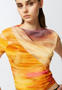 Top a manica corta con un design fluido in tonalità arancioni, gialle e viola, realizzato in tessuto leggero con una texture arricciata.