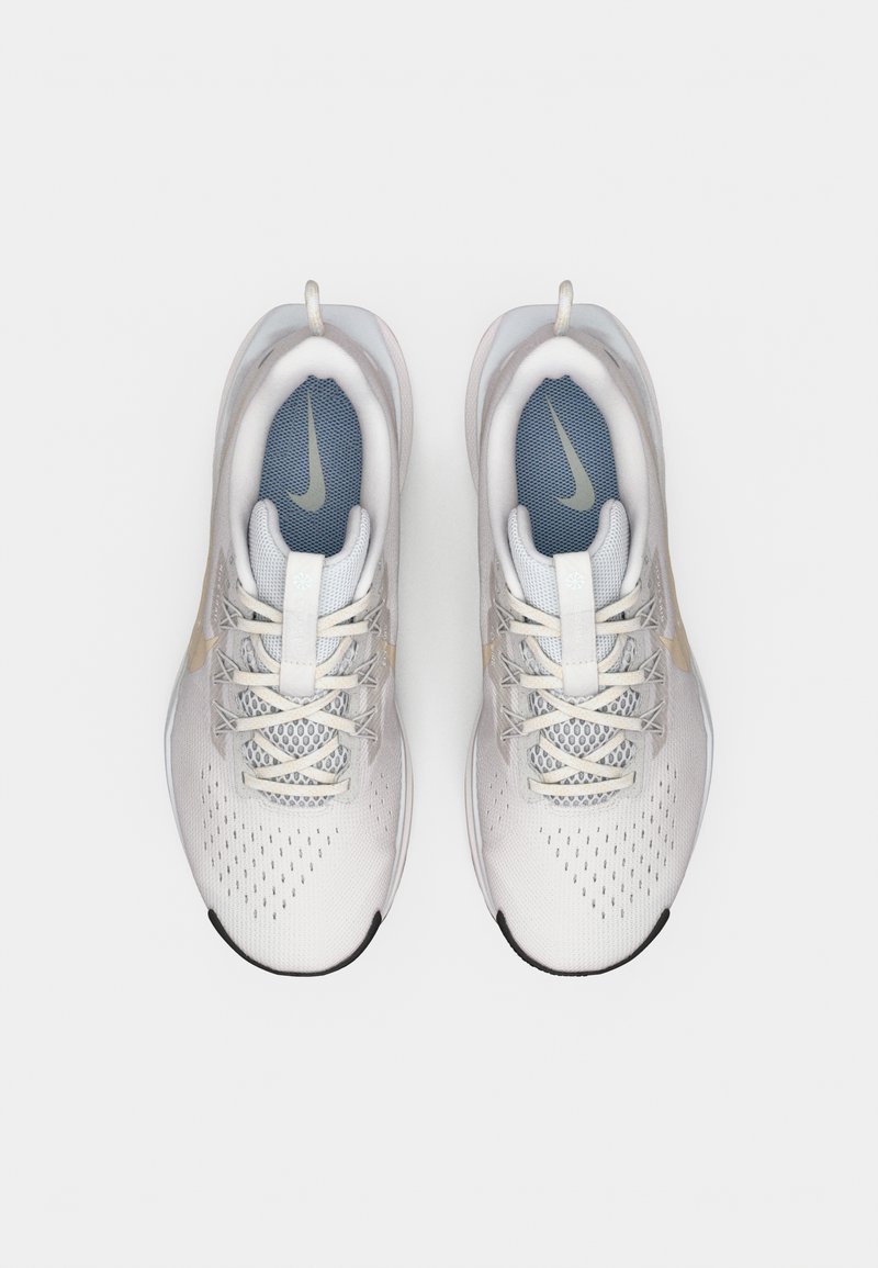 Par de zapatillas de correr Nike blancas y limpias con detalles en beige claro y plantillas azules, vistas desde arriba sobre un fondo blanco liso.