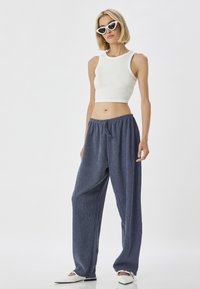 Un haut court à côtes blanc avec un pantalon large texturé bleu marine à taille élastique. Modèle portant des lunettes de soleil blanches en forme de chat et des chaussures plates.