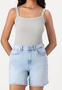 Top sin mangas de canalé gris combinado con pantalones cortos de mezclilla azul claro que presentan acentos en forma de corazón en los laterales y una cintura estándar con cierre de botón.