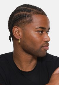 Gold drop earrings with a smooth, reflective surface worn by a person, displayed against a plain white background. The design is elongated and sleek.