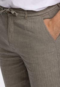 Pantalones grises con patrón de espiga y un acabado texturizado, presentan una cintura con cordón y bolsillos laterales. Detalle en primer plano de la tela y el ajuste.