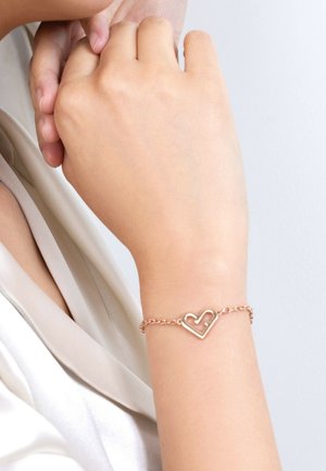 Bracelet en or rose avec un design en maillons de chaîne, présentant une forme de cœur ouvert comme accent principal. Texture lisse et finition polie.