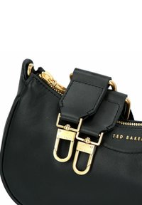 Schwarze Lederhandtasche mit Reißverschluss, zwei goldfarbenen Metalldetails und einer glatten Oberfläche. Enthält ein charakteristisches Logo-Detail.