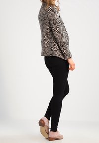 Blazer à imprimé zèbre en noir et beige, coupe ajustée, fermeture à un bouton, associé à des leggings noirs et des chaussures couleur blush.