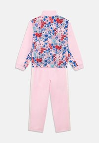 Tuta floreale con giacca rosa con zip decorata da fiori blu e rossi e pantaloni rosa abbinati con strisce bianche laterali. Tessuto morbido al tatto.