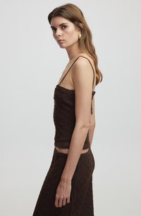 Top in maglia marrone con spalline sottili, caratterizzato da un motivo testurizzato. Il tessuto ha un aspetto leggermente rigato ed è abbinato a un indumento inferiore coordinato.