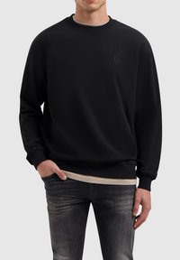 Zwarte sweatshirt met een ronde hals, lange mouwen en ribgebreide boorden. Heeft een reliëf logo op de borst en is gemaakt van zachte stof.