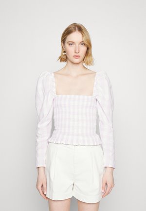 Top de mangas bufantes em tecido xadrez roxo claro com design franzido e bainha com volantes. Combinado com calções plissados brancos.