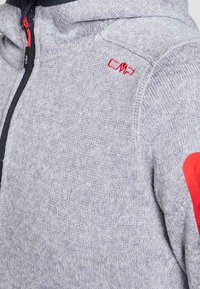 Grijze gebreide hoodie met een volledige ritssluiting, zwarte accenten en rode elleboogpatches. Beschikt over een gestructureerde stof en het CMP-logo op de schouder.