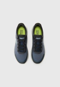 Blaue und schwarze Sportschuhe mit Mesh-Obermaterial, runder Zehenform und Schnürdesign. Sie verfügen über eine grüne Einlegesohle und eine hellfarbige kontrastierende Sohle.