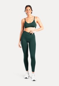 Zielony sportowy komplet składający się z dopasowanego crop topu na cienkich ramiączkach oraz legginsów z wysokim stanem, oba wykonane z gładkiego, elastycznego materiału.