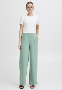 Lichte witte geribde top met korte ruches mouwen, gecombineerd met hoge taille, wijde mintgroene broeken met voorplooien.