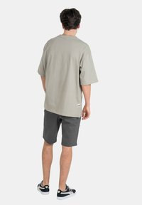 Light gray oversized t-shirt with short sleeves, paired with dark gray shorts. Model wears black sneakers with white soles. Minimal branding visible.