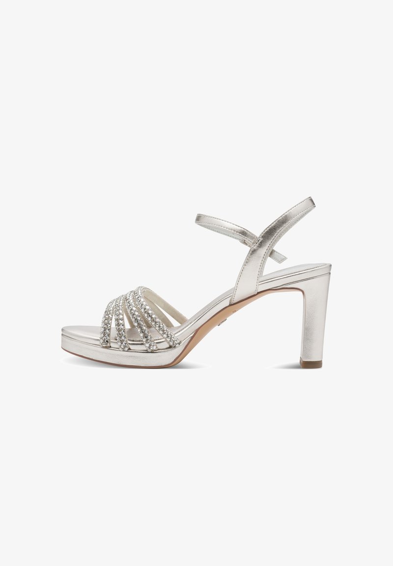 Ασημί πέδιλο με ψηλό τακούνι, λουράκι στον αστράγαλο και πέντε λουράκια μπροστά διακοσμημένα με στρας, ανοιχτή μύτη και τετράγωνο τακούνι.