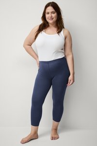 Marineblauwe leggings van soepel, rekbaar materiaal, gecombineerd met een witte tanktop. De leggings hebben een smalle, cropped pasvorm zonder patronen.