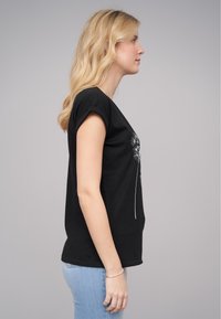 Svart bomulls t-skjorte med korte ermer, med et dandelion-motiv i hvitt på forsiden. Stylet med blå jeans.